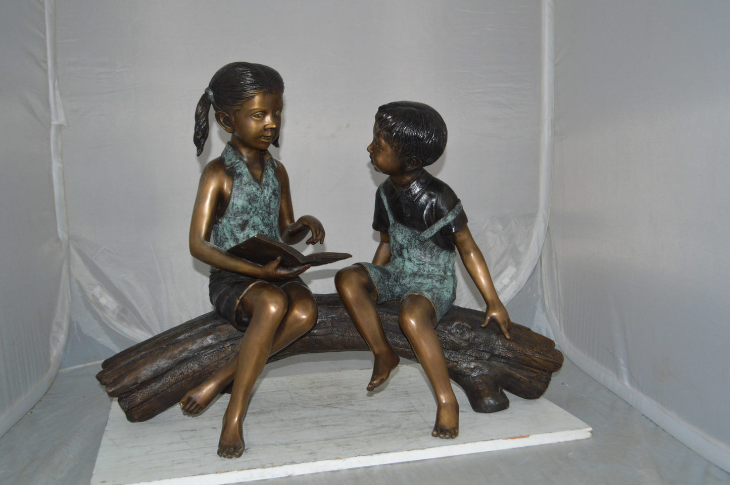Boy and Girl on a tree log reading Bronze Statue - Size: 37"L x 14"W x 27"H.