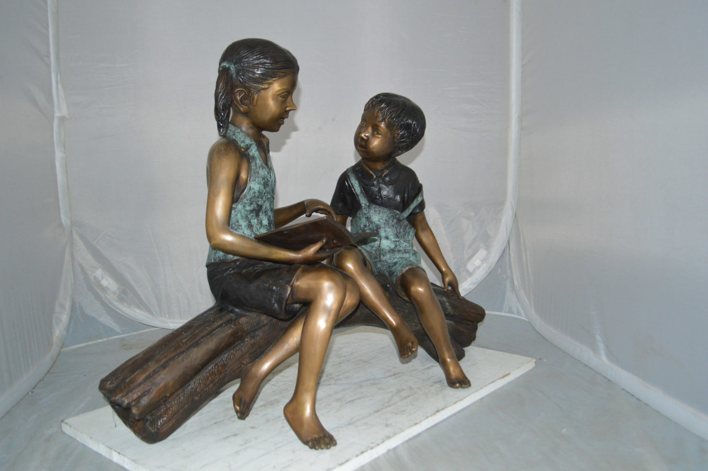 Boy and Girl on a tree log reading Bronze Statue - Size: 37"L x 14"W x 27"H.