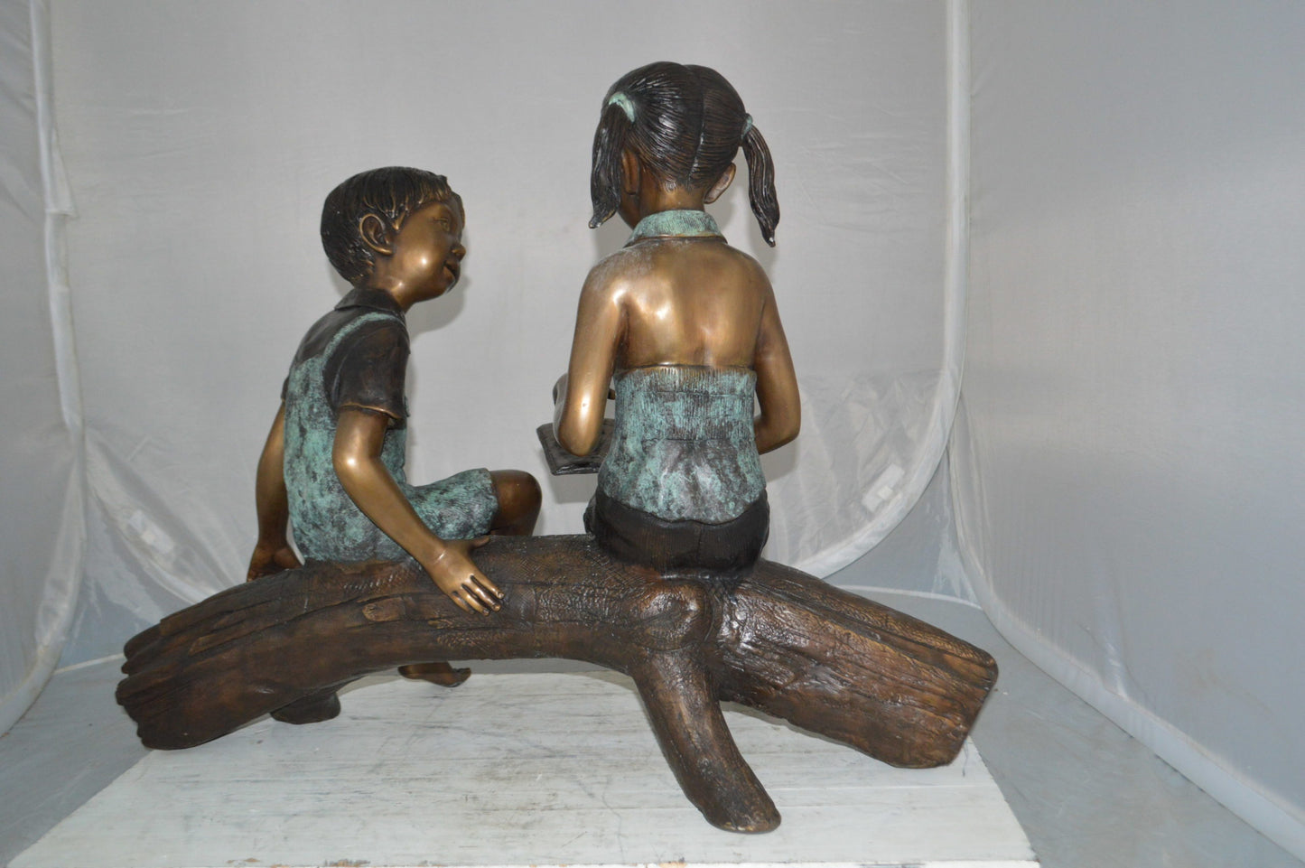 Boy and Girl on a tree log reading Bronze Statue - Size: 37"L x 14"W x 27"H.