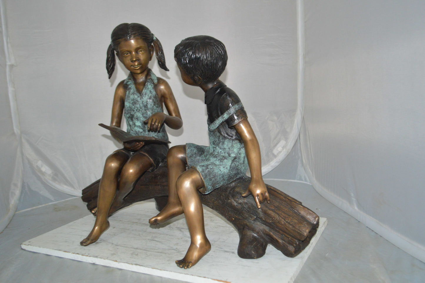 Boy and Girl on a tree log reading Bronze Statue - Size: 37"L x 14"W x 27"H.