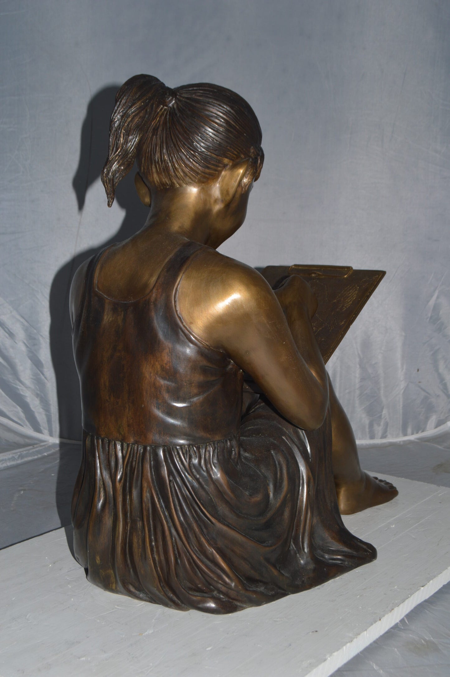 Girl reading from a notebook Bronze Statue - Size: 26"L x 16"W x 25"H.