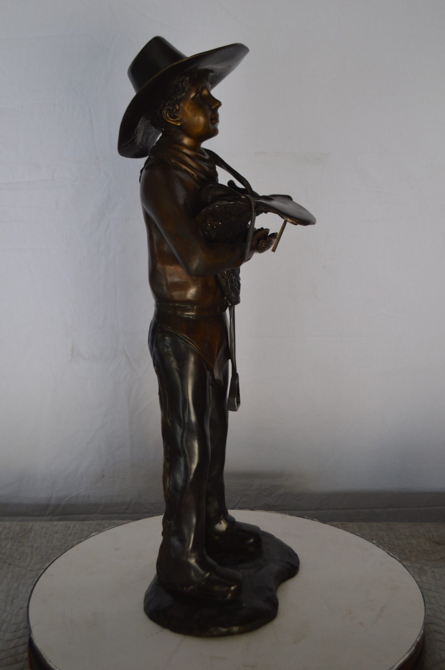 Cowboy Holding a Saddle Bronze Statue  -  Size: 12"L x 11"W x 32"H.