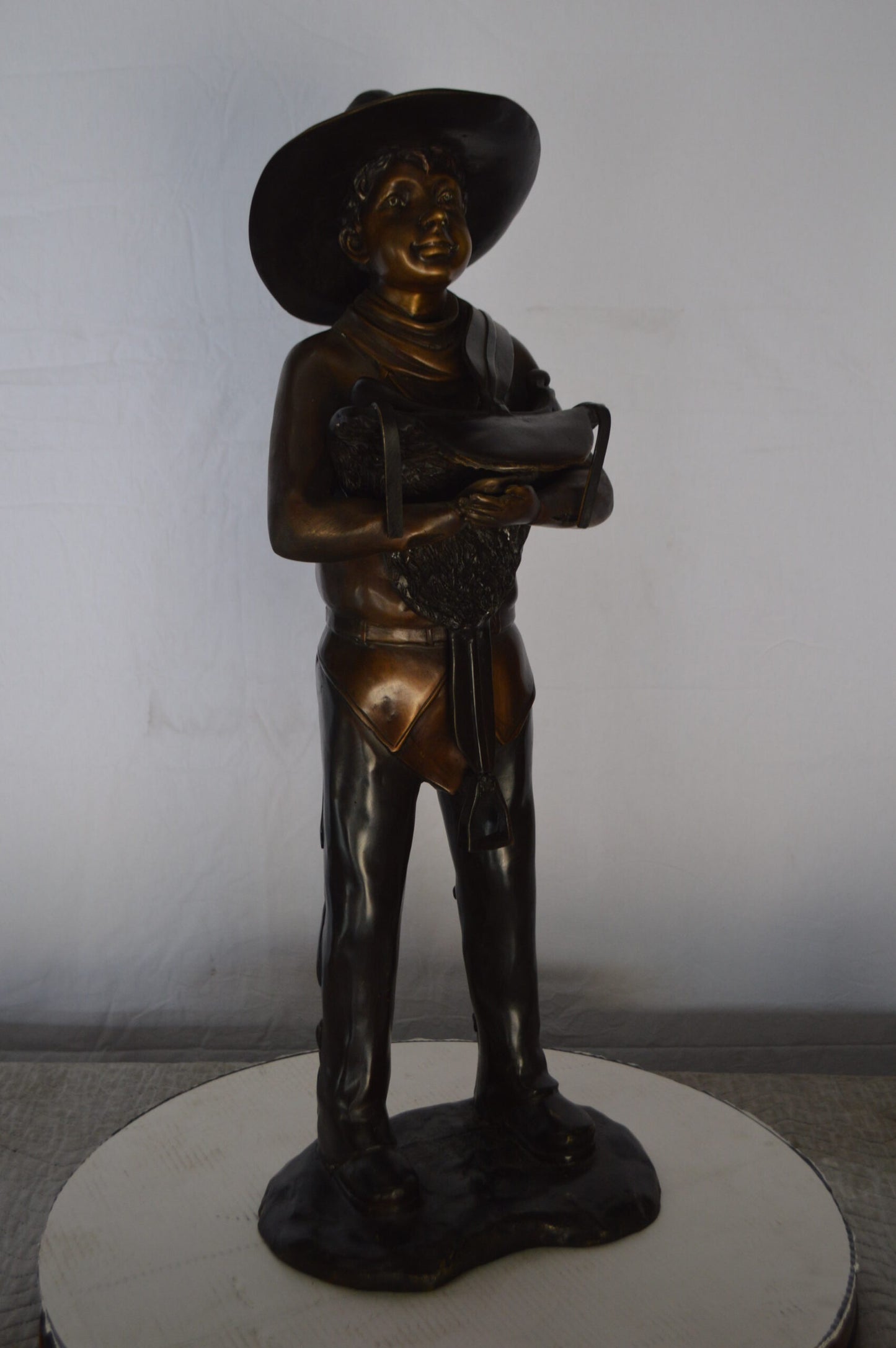 Cowboy Holding a Saddle Bronze Statue - Size: 12"L x 11"W x 32"H.