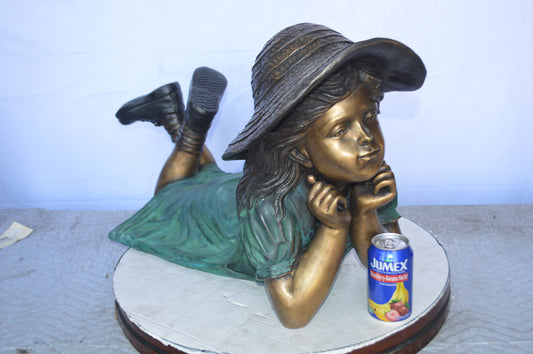Girl Wearing A Hat Lying on Stomach Bronze Statue - Size: 33"L x 17"W x 17"H.