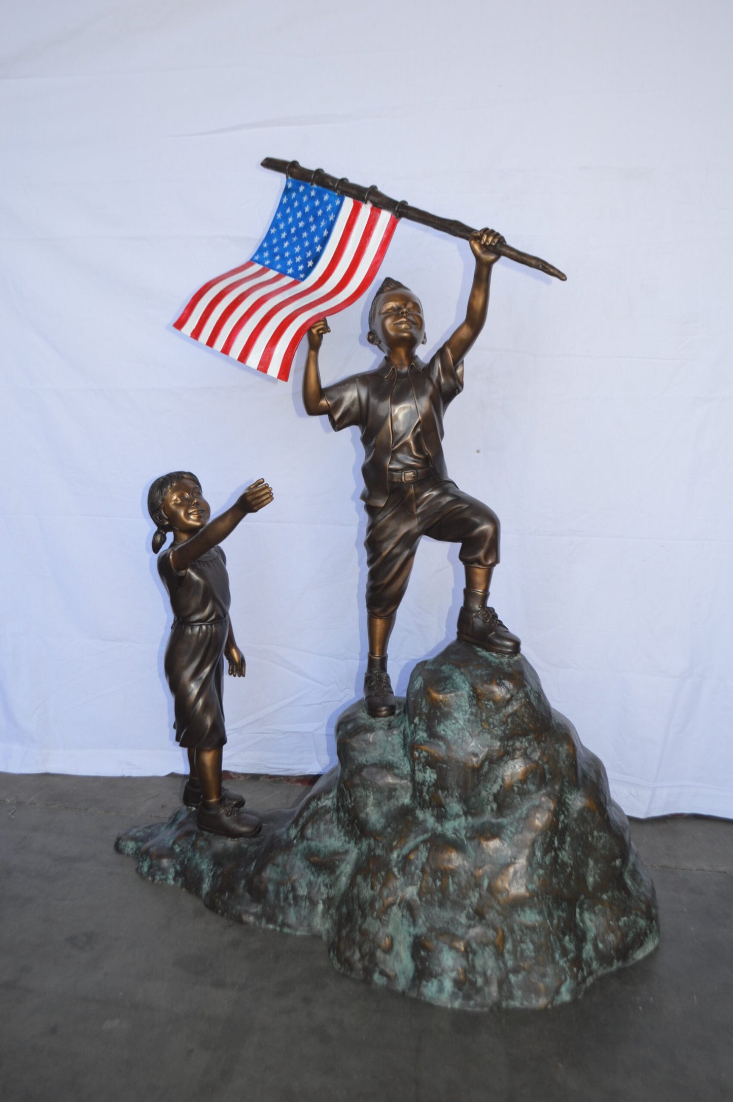 Two Kids on Rock W the American Flag Bronze Statue - Size: 50"L x 22"W x 58"H.