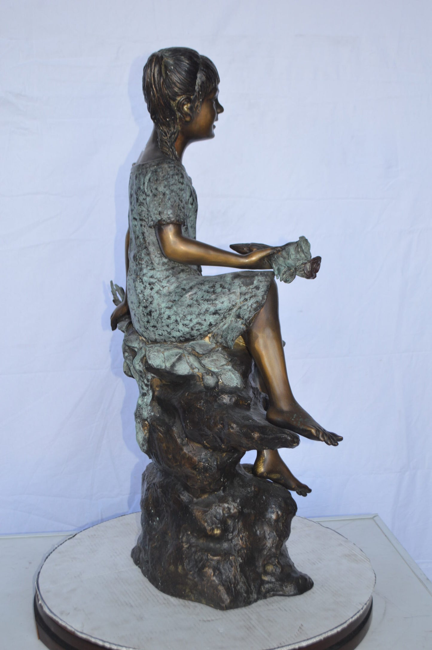 Girl on Tree Trunk Holding Flowers Bronze Statue - Size: 26"L x 11"W x 36"H.