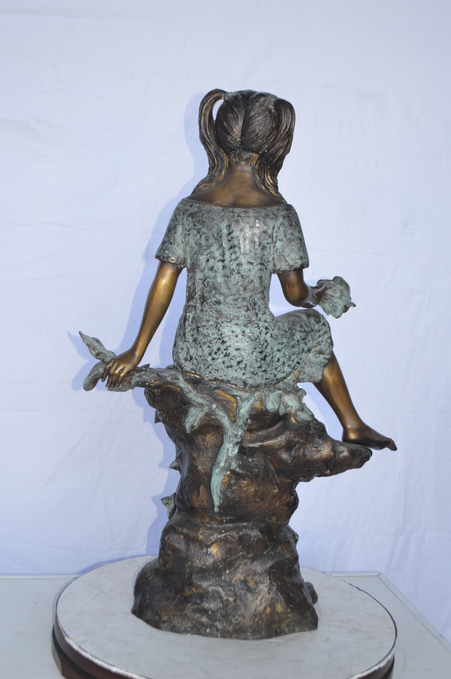 Girl on Tree Trunk Holding Flowers Bronze Statue - Size: 26"L x 11"W x 36"H.