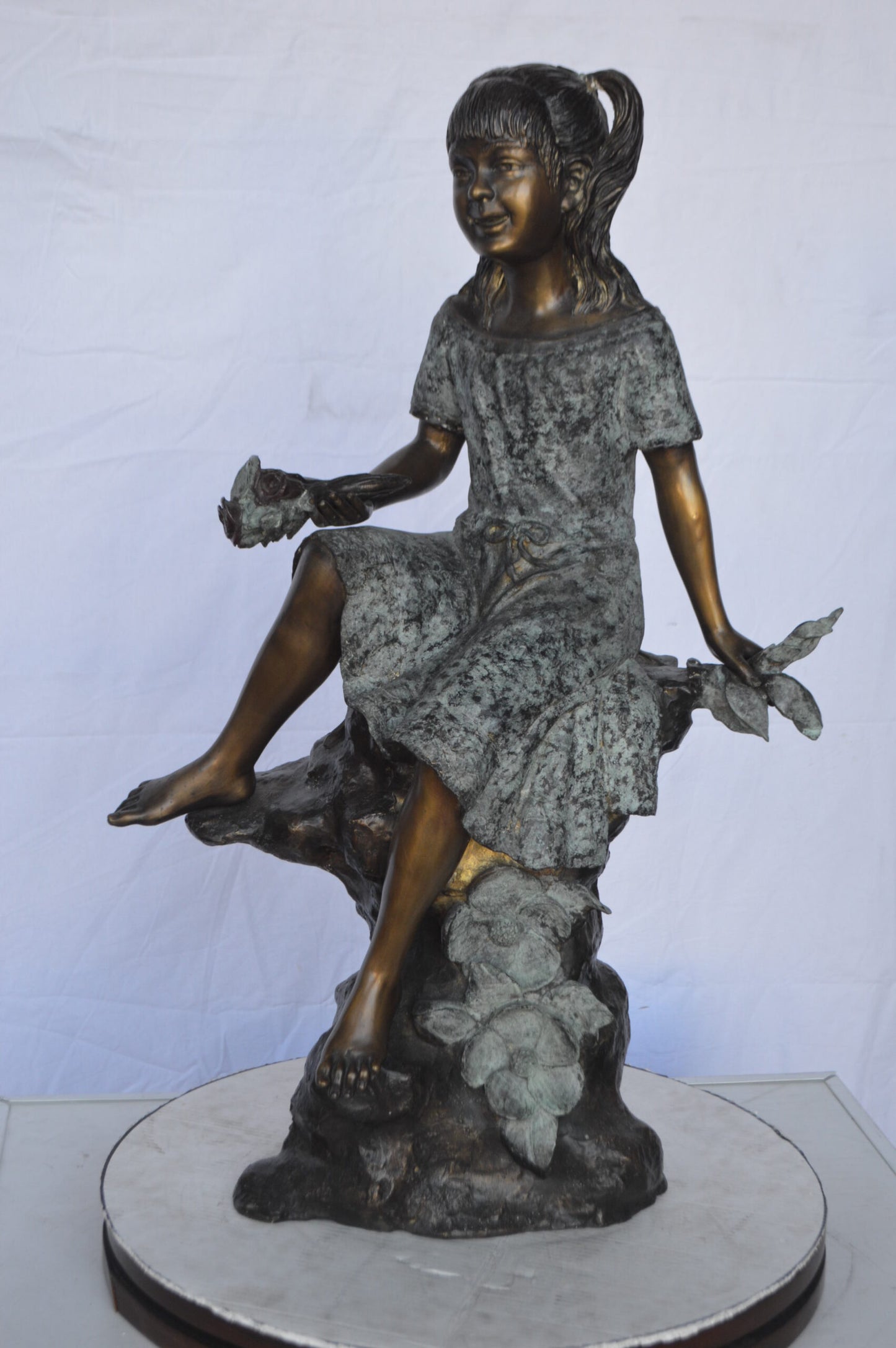 Girl on Tree Trunk Holding Flowers Bronze Statue - Size: 26"L x 11"W x 36"H.