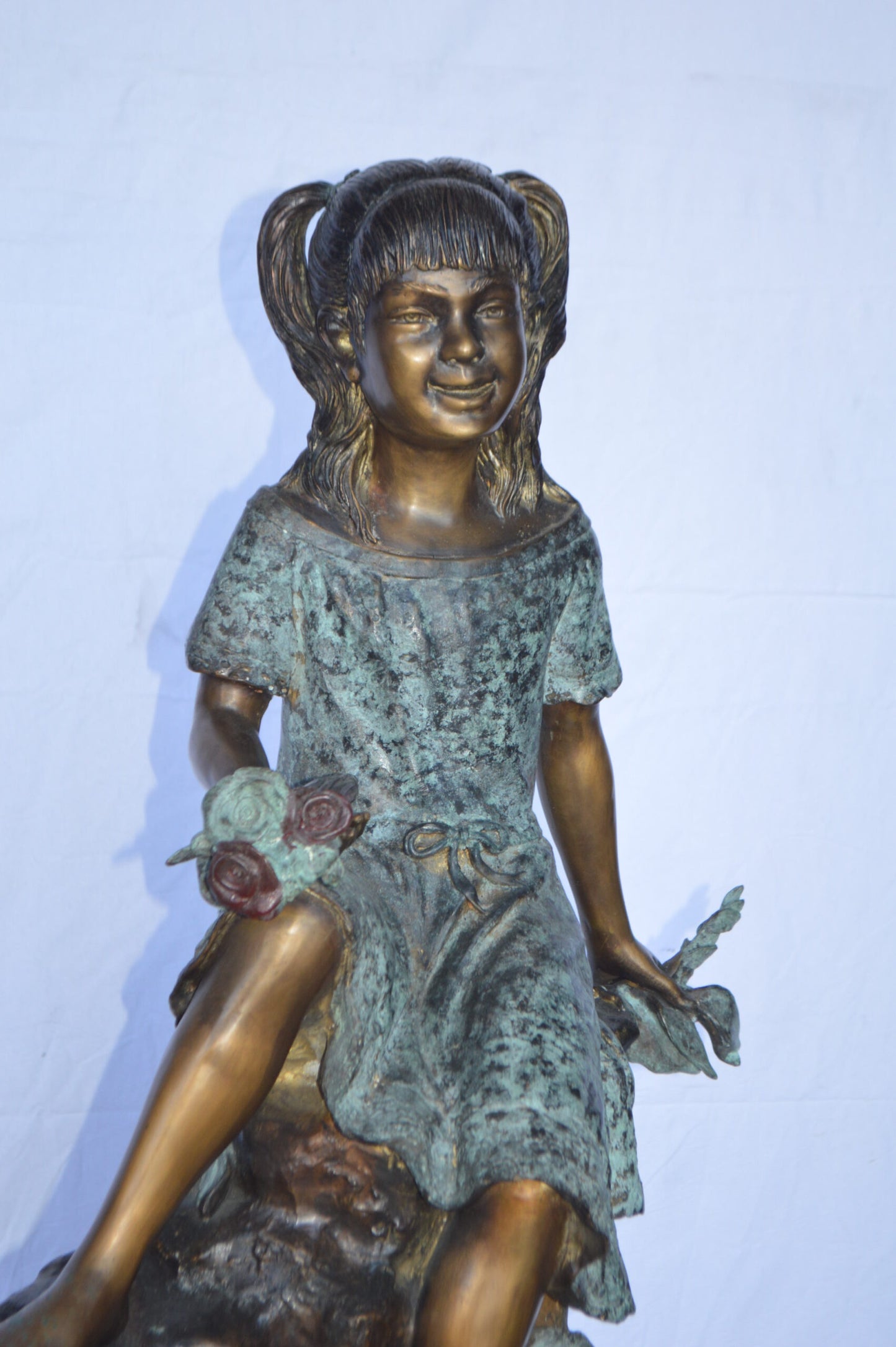 Girl on Tree Trunk Holding Flowers Bronze Statue - Size: 26"L x 11"W x 36"H.