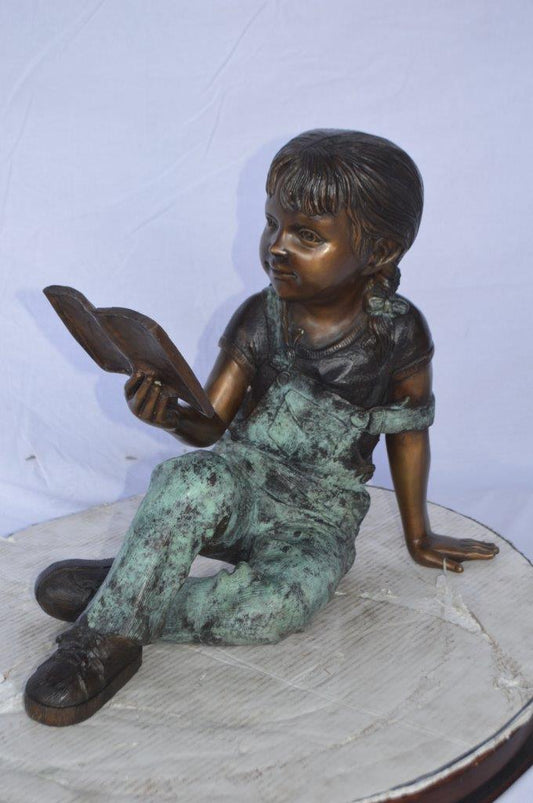 Young girl laying and reading book bronze statue - Size: 18"L x 9"W x 16"H.