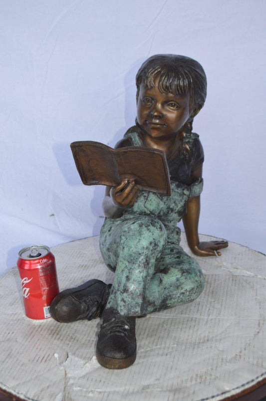 Young girl laying and reading book bronze statue - Size: 18"L x 9"W x 16"H.