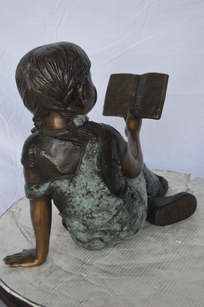 Young girl laying and reading book bronze statue -  Size: 18"L x 9"W x 16"H.