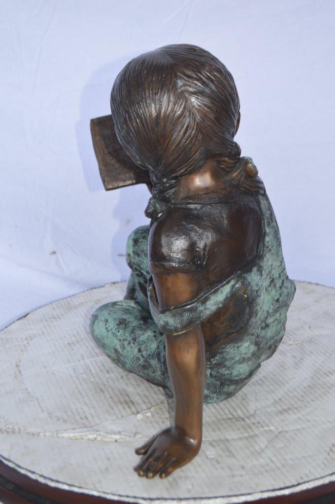Young girl laying and reading book bronze statue -  Size: 18"L x 9"W x 16"H.