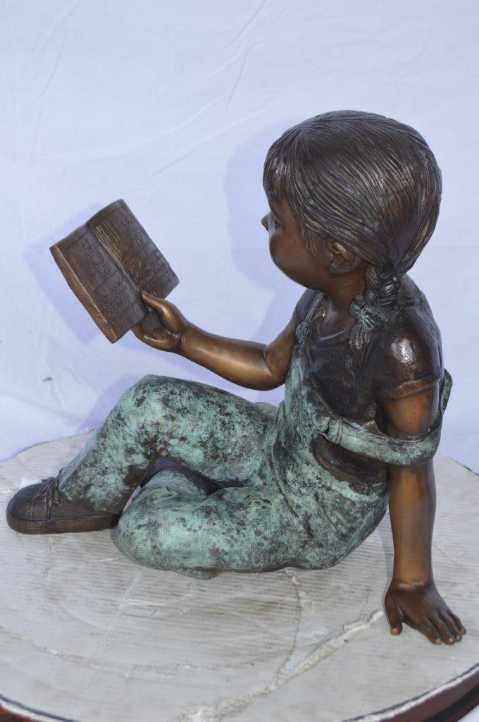 Young girl laying and reading book bronze statue -  Size: 18"L x 9"W x 16"H.