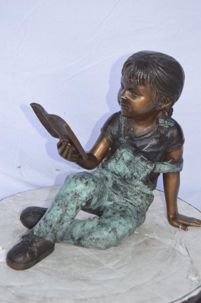 Young girl laying and reading book bronze statue -  Size: 18"L x 9"W x 16"H.