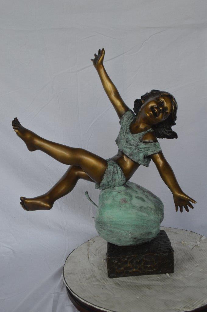 Girl having fun on apple bronze statue - Size: 22"L x 9"W x 31"H.