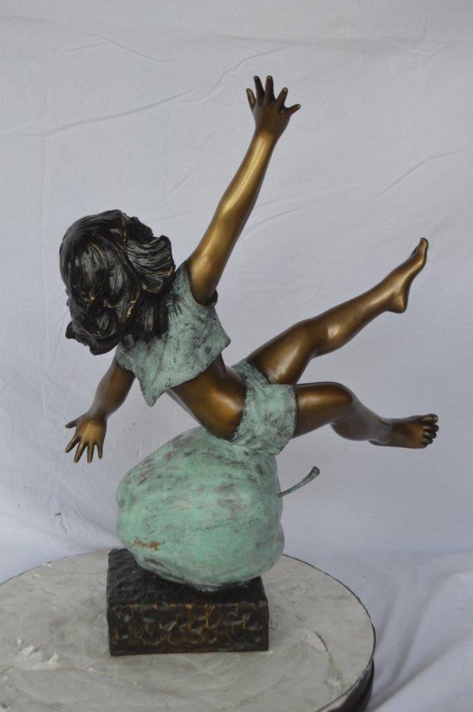 Girl having fun on apple bronze statue -  Size: 22"L x 9"W x 31"H.