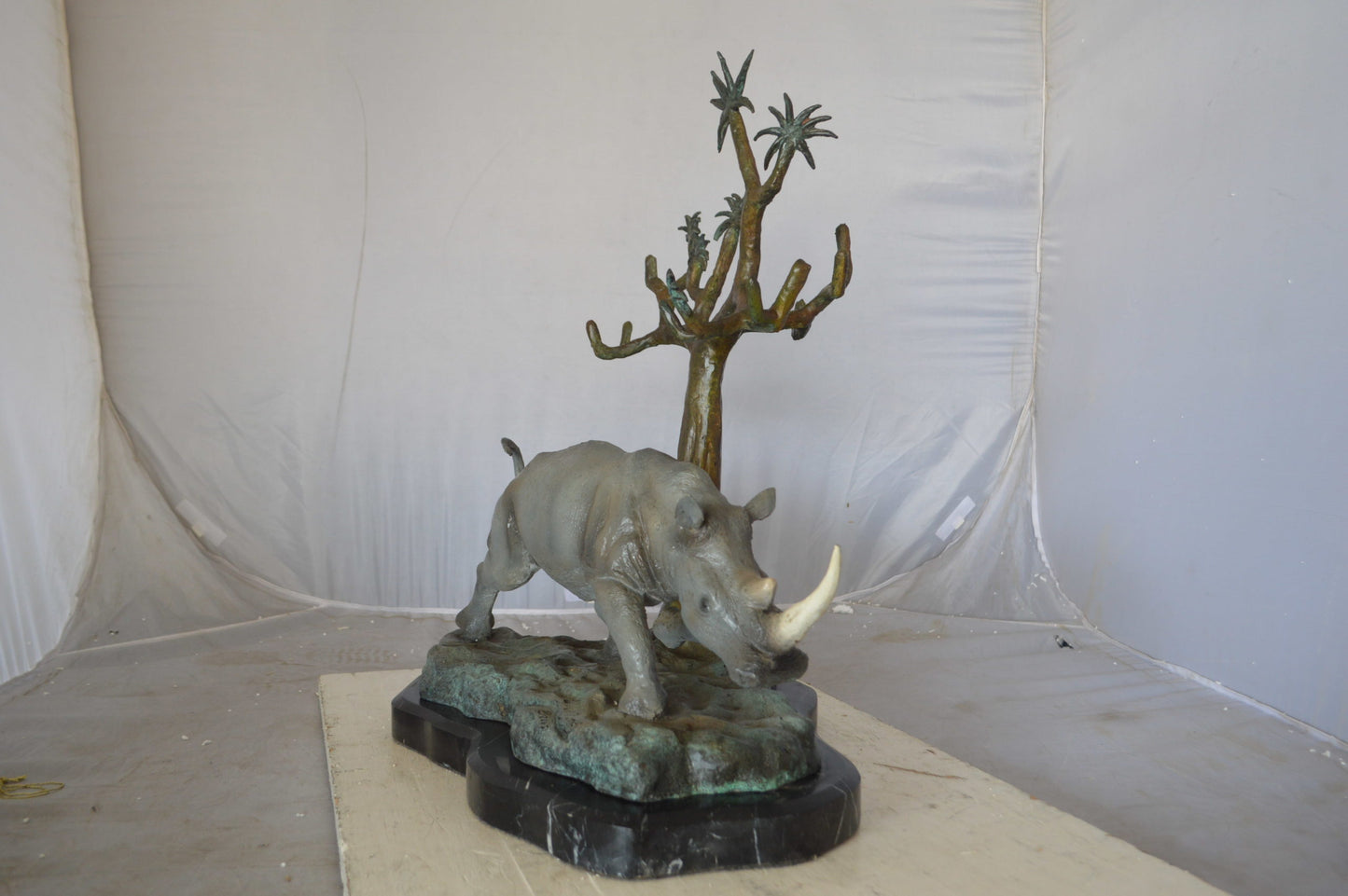 Rhino Relaxed under a tree bronze statue - Size: 22"L x 15"W x 25"H.