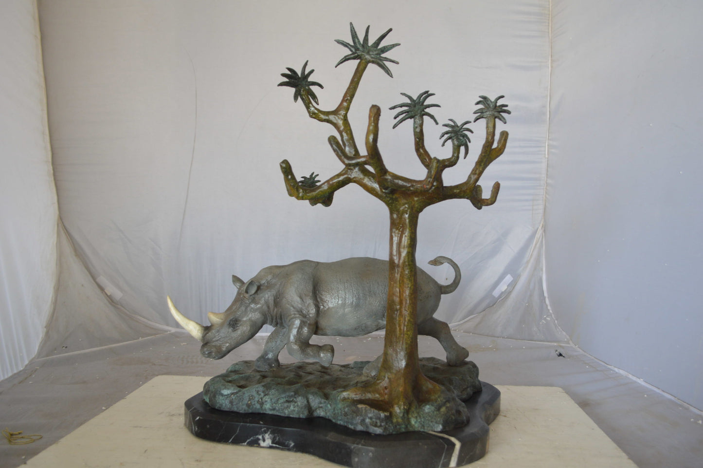 Rhino Relaxed under a tree bronze statue - Size: 22"L x 15"W x 25"H.