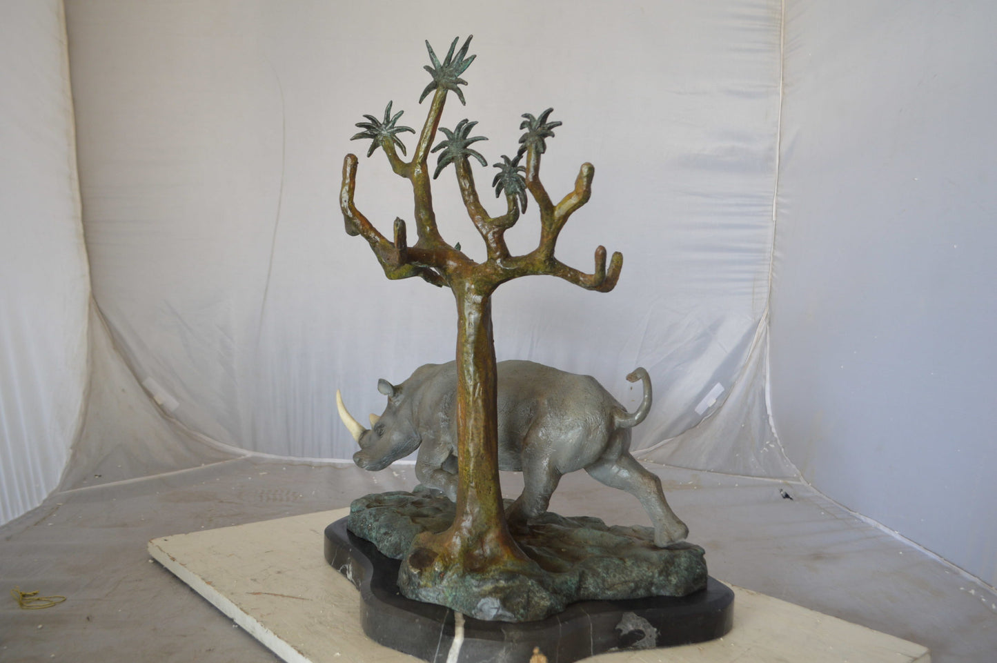 Rhino Relaxed under a tree bronze statue - Size: 22"L x 15"W x 25"H.