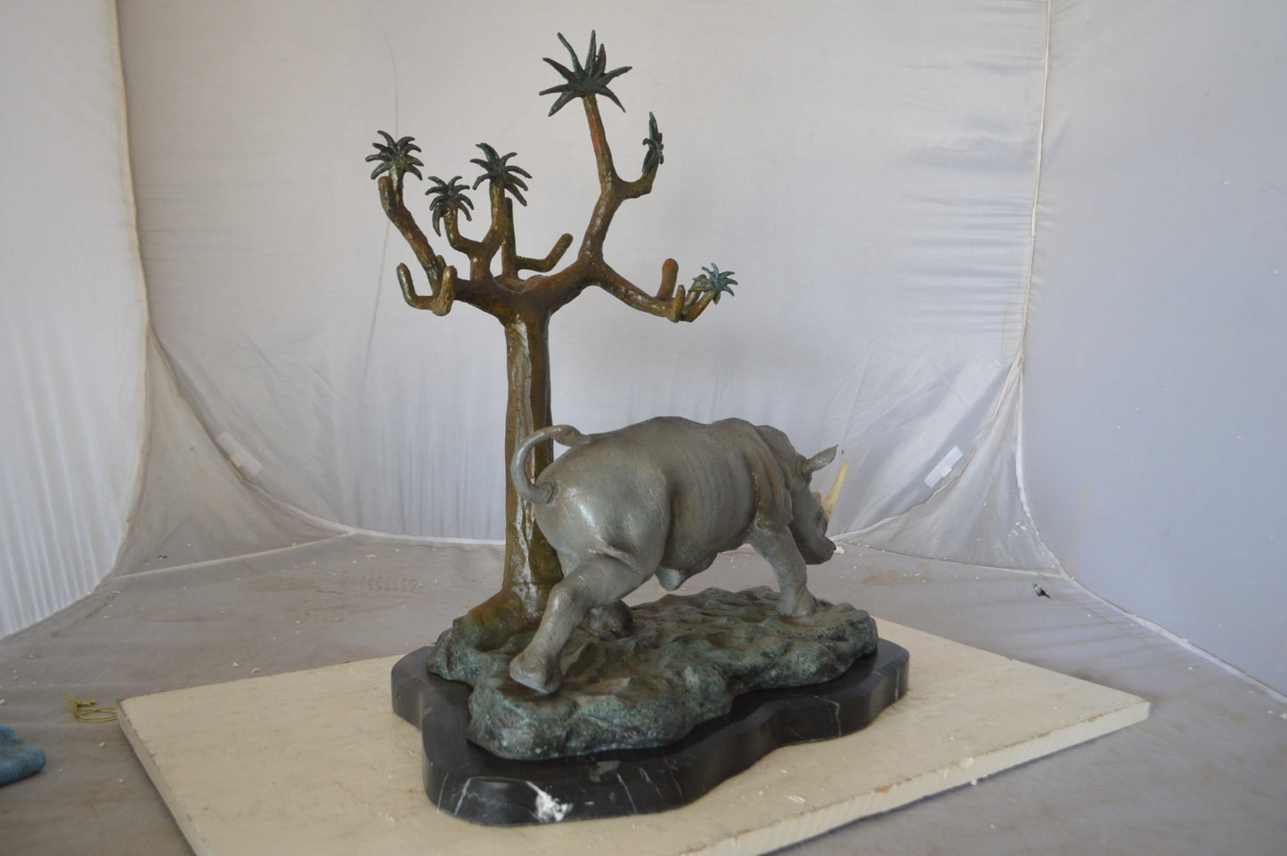 Rhino Relaxed under a tree bronze statue - Size: 22"L x 15"W x 25"H.