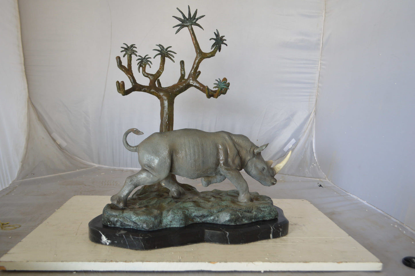 Rhino Relaxed under a tree bronze statue - Size: 22"L x 15"W x 25"H.