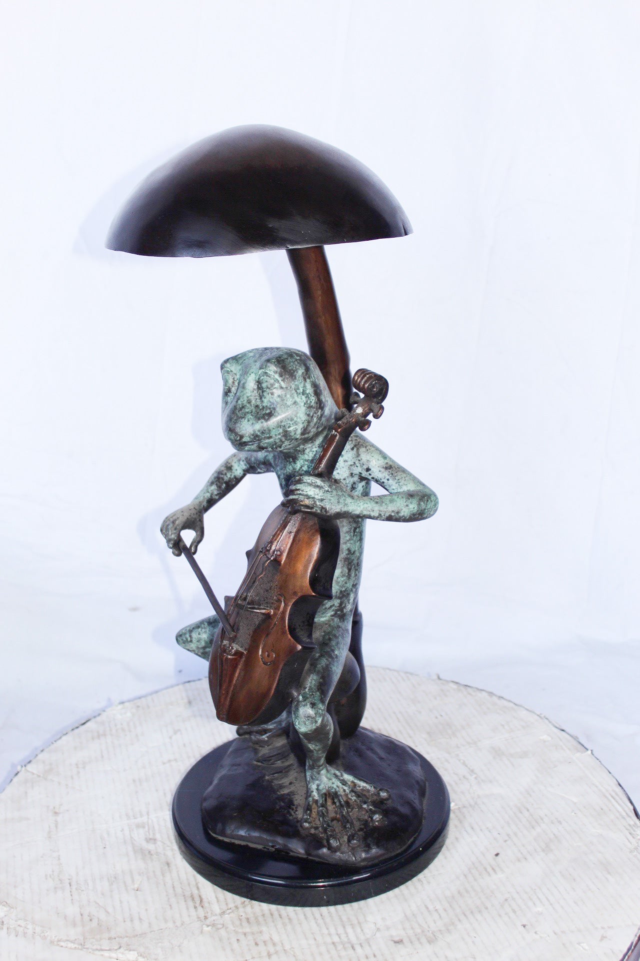 Frog playing cello under mushroom bronze statue - Size: 10"L x 10"W x 24"H.