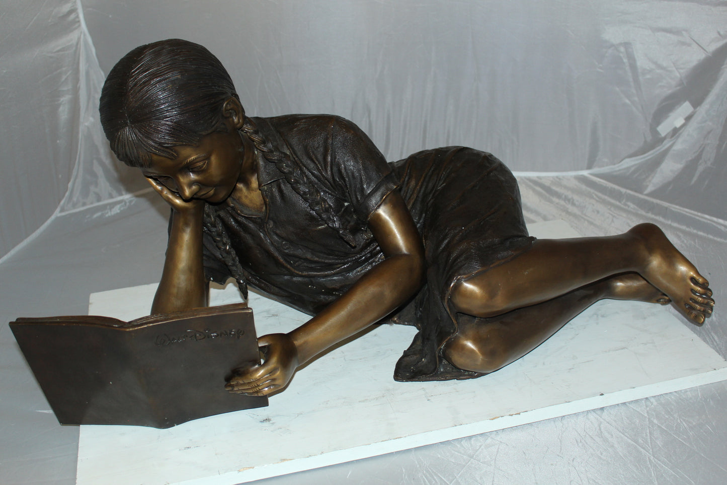 Girl laying reading a book Bronze Statue - Size: 36"L x 17"W x 18"H.
