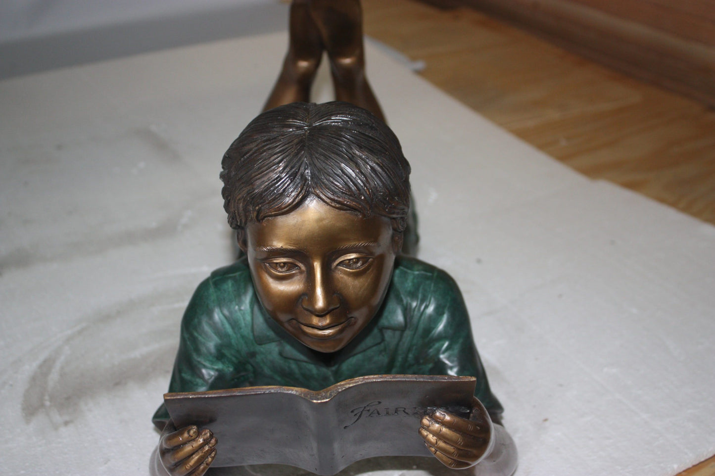 boy laying reading book bronze Statue - Size: 24"L x 10"W x 11"H.