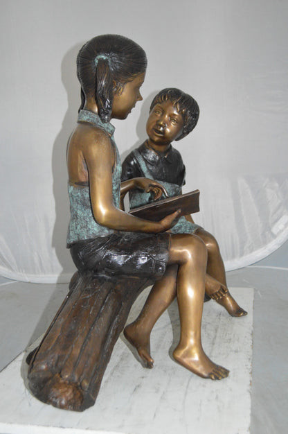 Boy and Girl on a tree log reading Bronze Statue -  Size: 37"L x 14"W x 27"H.
