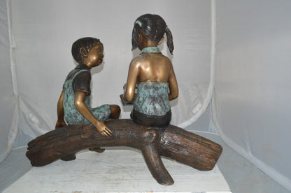 Boy and Girl on a tree log reading Bronze Statue -  Size: 37"L x 14"W x 27"H.