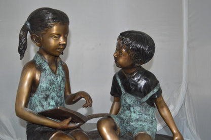 Boy and Girl on a tree log reading Bronze Statue -  Size: 37"L x 14"W x 27"H.