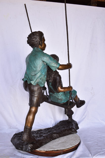 Boy and Girl Playing on a Swing bronze Statue - Size: 39"L x 17"W x 53"H.