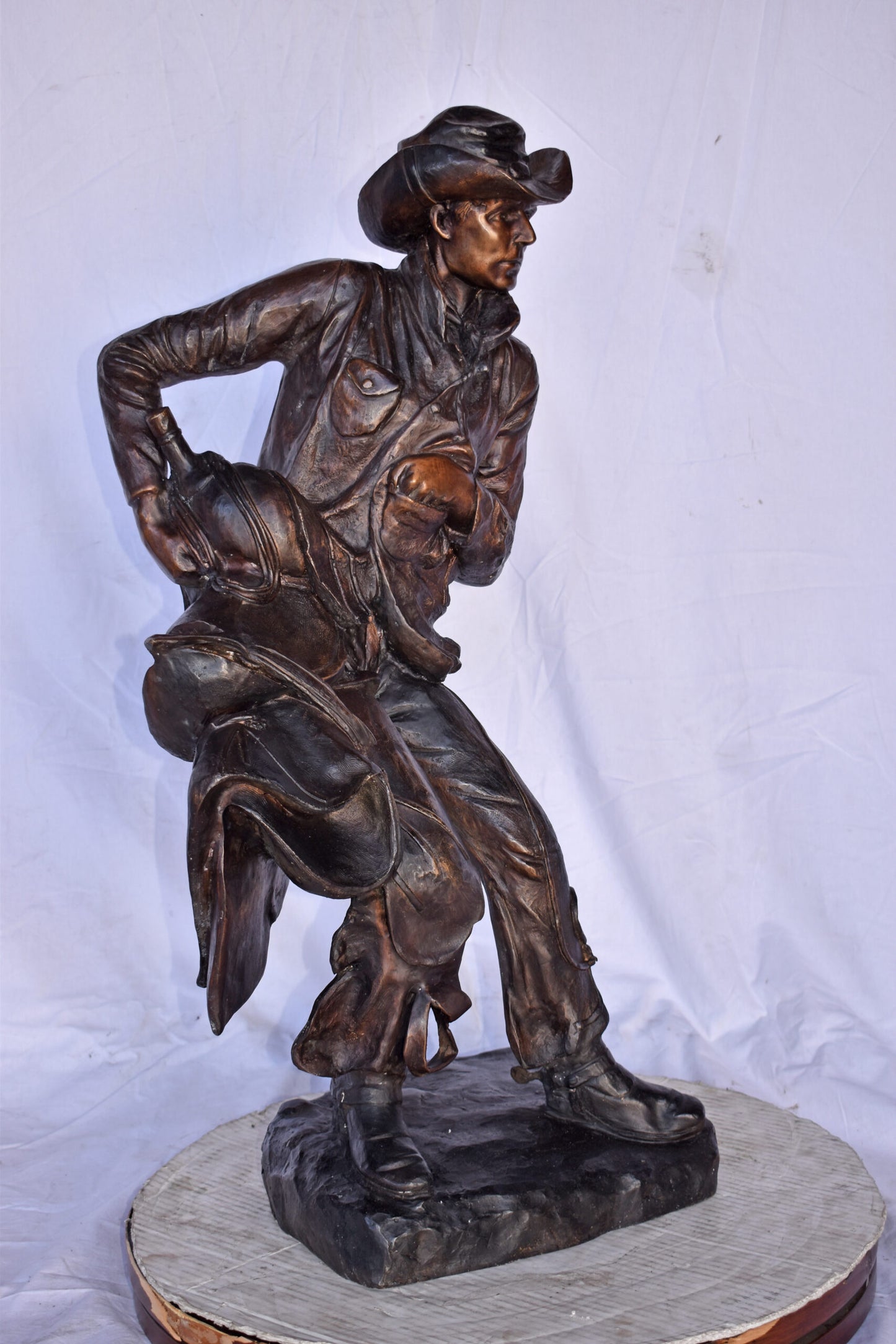 Cowboy Holding His Saddle Bronze Statue - Size: 20"L x 14"W x 35"H.