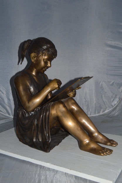 Girl reading from a notebook Bronze Statue -  Size: 26"L x 16"W x 25"H.
