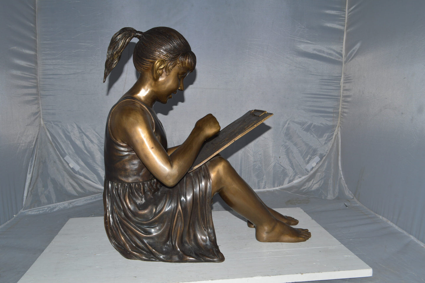 Girl reading from a notebook Bronze Statue -  Size: 26"L x 16"W x 25"H.