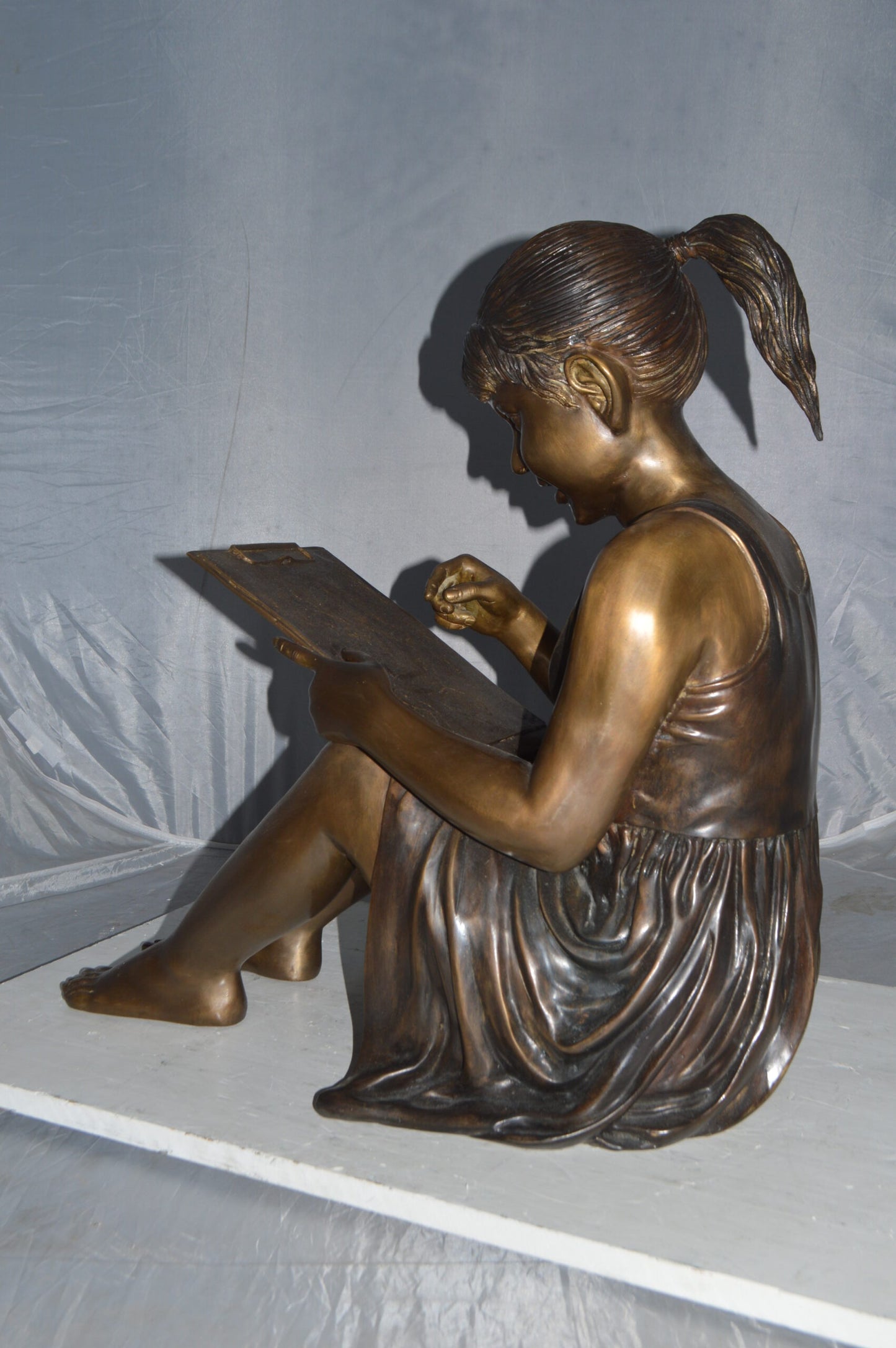 Girl reading from a notebook Bronze Statue -  Size: 26"L x 16"W x 25"H.