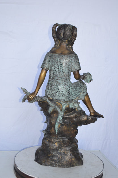Girl on Tree  Trunk Holding Flowers Bronze Statue -  Size: 26"L x 11"W x 36"H.