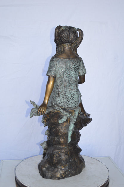 Girl on Tree  Trunk Holding Flowers Bronze Statue -  Size: 26"L x 11"W x 36"H.
