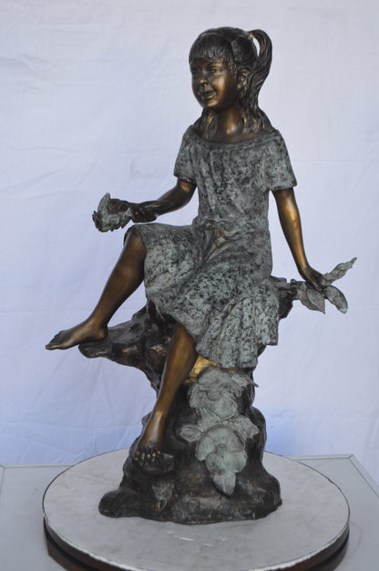 Girl on Tree  Trunk Holding Flowers Bronze Statue -  Size: 26"L x 11"W x 36"H.