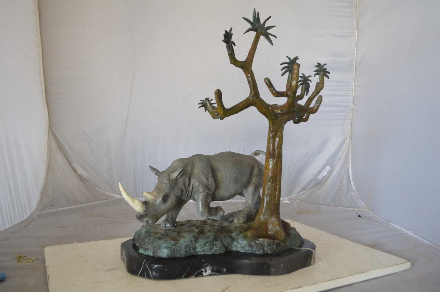 Rhino Relaxed under a tree bronze statue - Size: 22"L x 15"W x 25"H.