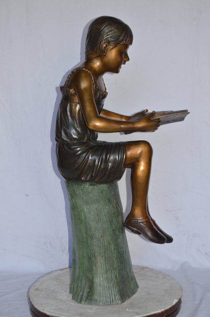 Girl Sitting on a Tree Stump, Reading Bronze Statue - Size: 15"L x 20"W x 22"H.