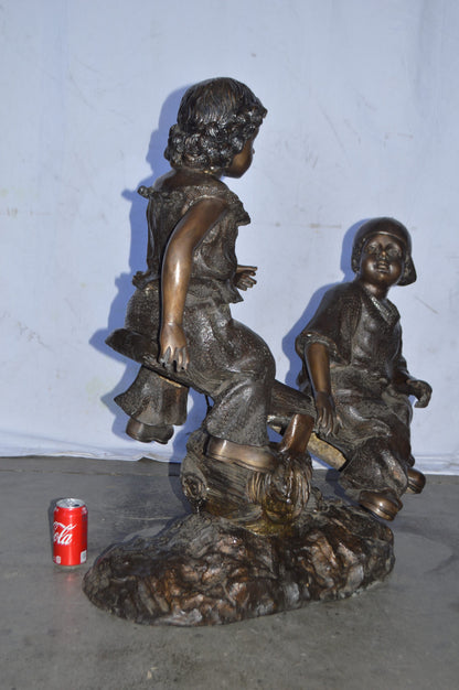 A Boy and a Girl Playing Seesaw Bronze Statue - Size: 17"L x 33"W x 36"H.
