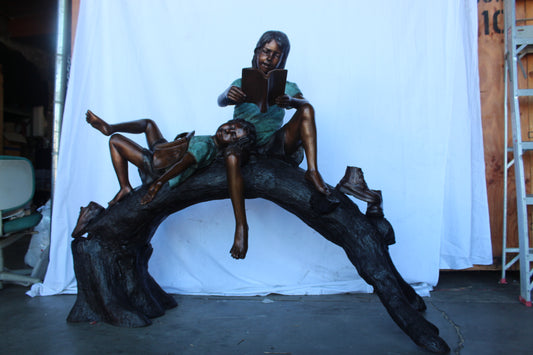 Boy and girl reading on arched tree bronze statue  -  Size: 70"L x 29"W x 56"H.
