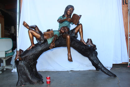 Boy and girl reading on arched tree bronze statue  -  Size: 70"L x 29"W x 56"H.