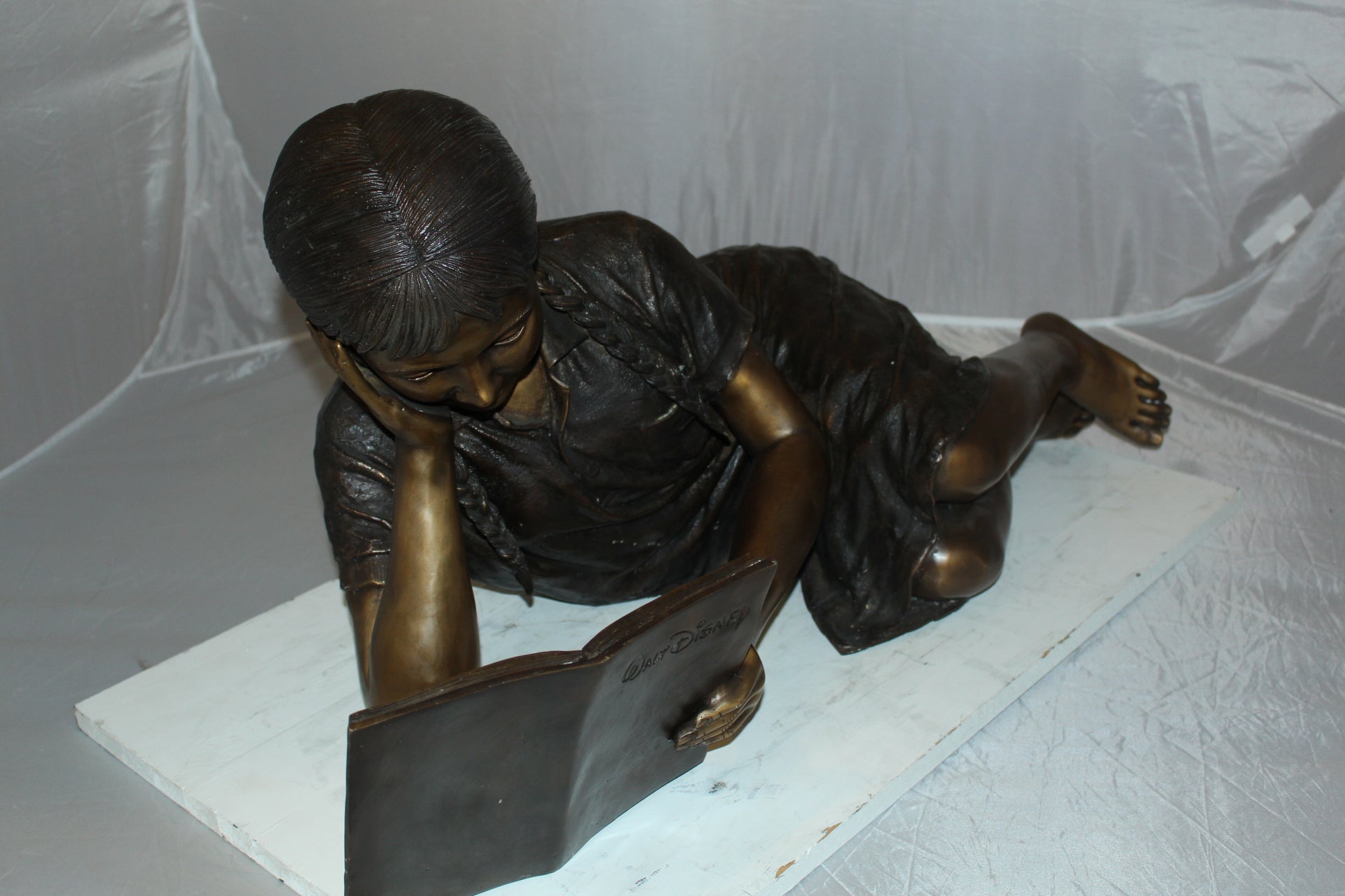 Girl laying reading a book Bronze Statue -  Size: 36"L x 17"W x 18"H. 