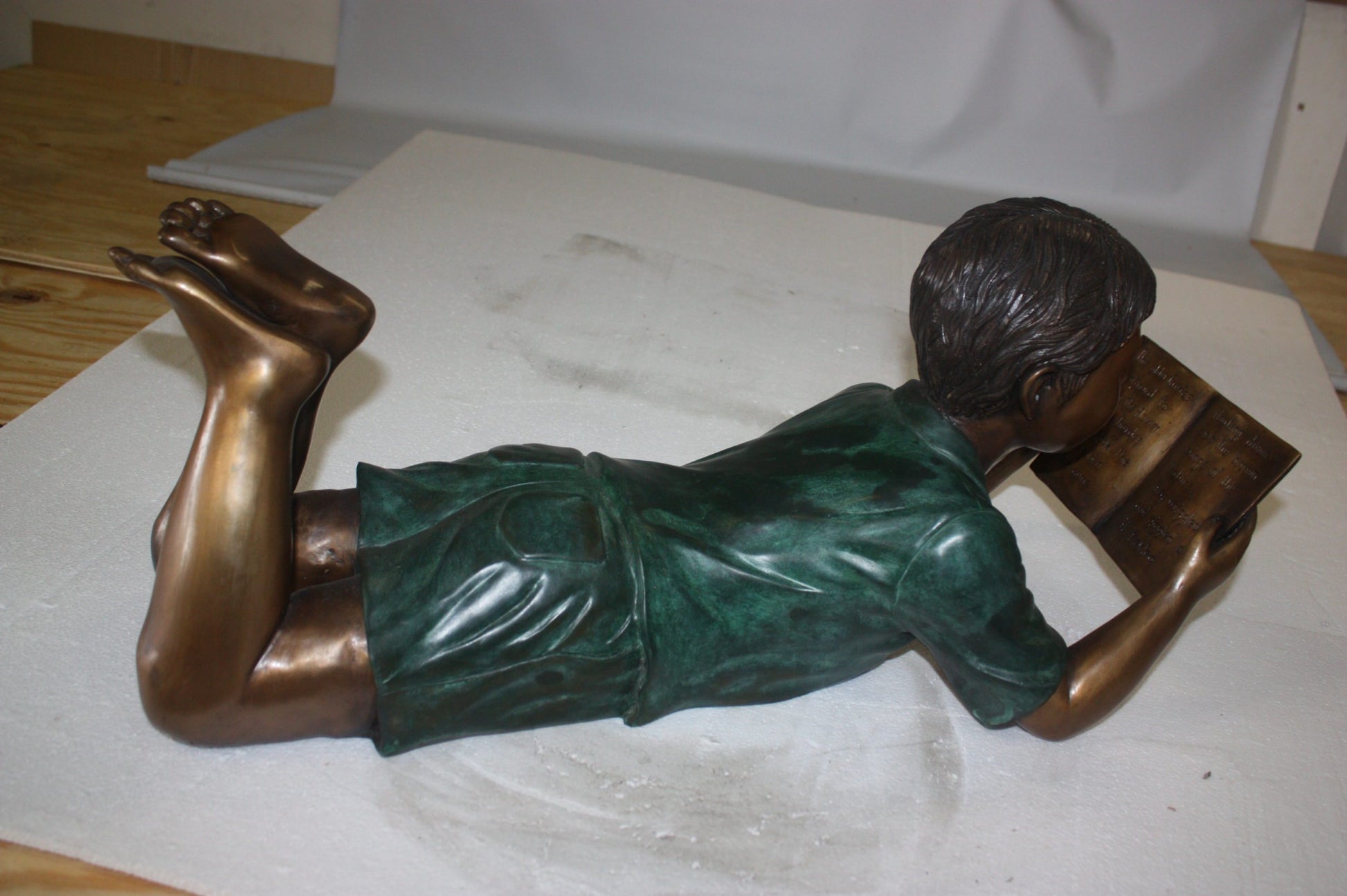 boy laying reading book bronze Statue -  Size: 24"L x 10"W x 11"H. 