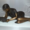 Girl laying reading a book Bronze Statue -  Size: 36"L x 17"W x 18"H.