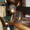 Girl laying on a bench reading a book Bronze Statue -  Size: 27"L x 39"W x 32"H