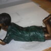 boy laying reading book bronze Statue -  Size: 24"L x 10"W x 11"H.